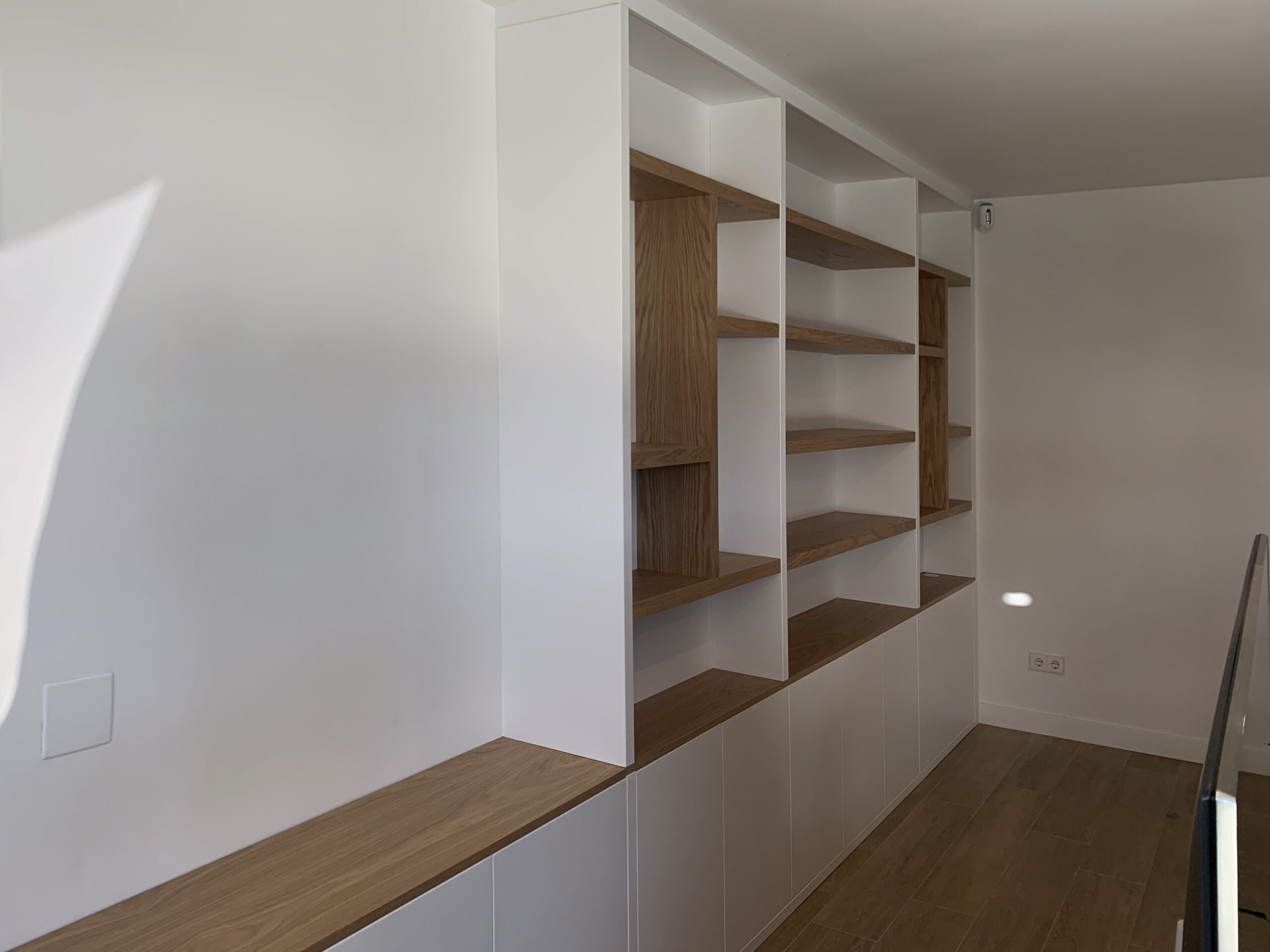 Vista lateral de mueble a medida para salón con librería combinado blanco y madera