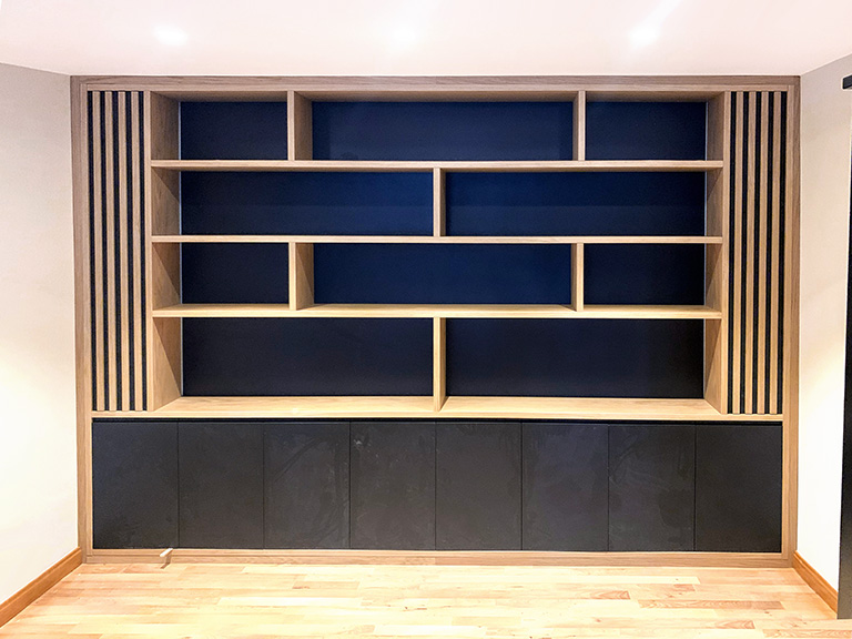 Librería mural lacada en blanco con puertas y cajones, estantes en madera de haya y espejo integrado