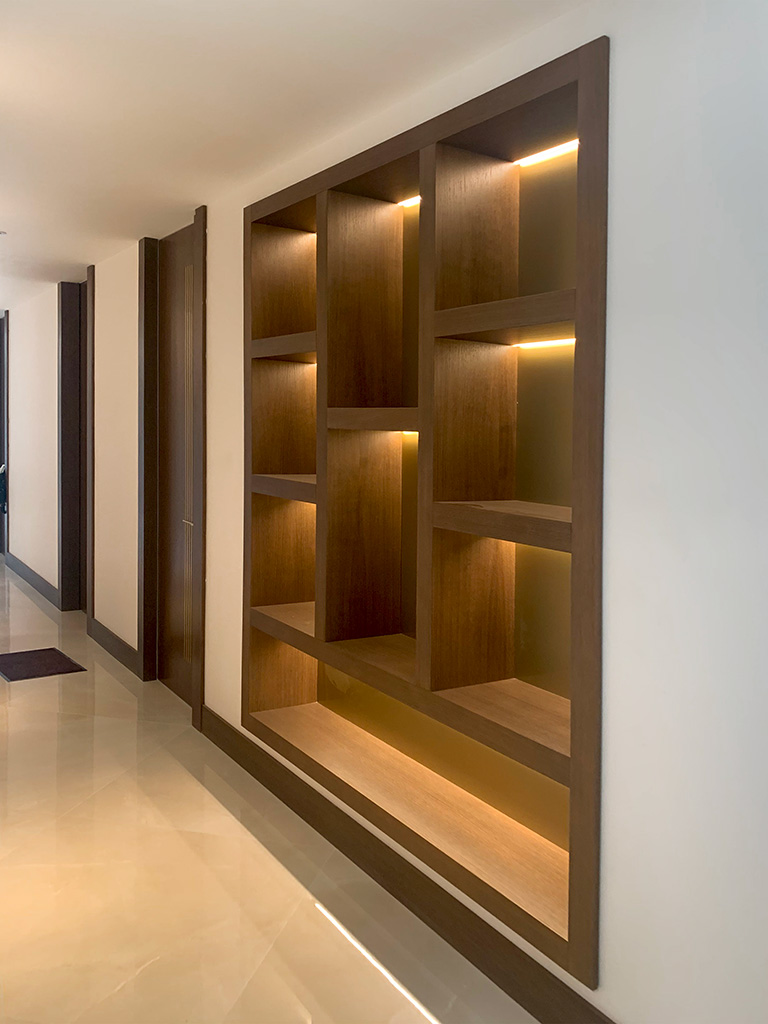 Librería mural lacada en blanco con puertas y cajones, estantes en madera de haya y espejo integrado