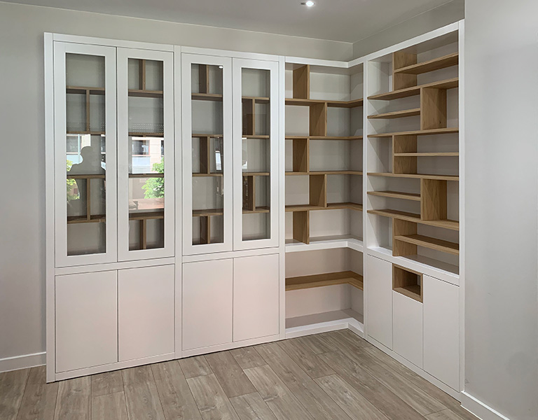 Librería mural lacada en blanco con puertas y cajones, estantes en madera de haya y espejo integrado
