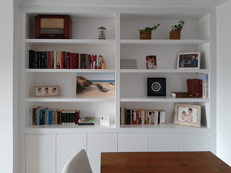 Librería mural lacada en blanco con puertas y cajones, estantes en madera de haya y espejo integrado