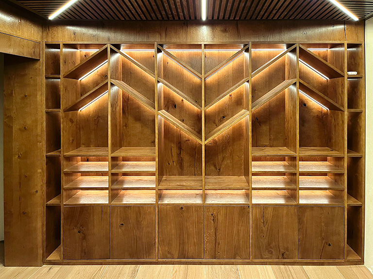 Librería mural lacada en blanco con puertas y cajones, estantes en madera de haya y espejo integrado